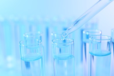 Dripping liquid from pipette into test tube on light blue background, closeup