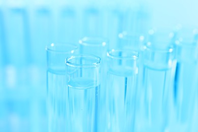 Photo of Many glass test tubes on light blue background, closeup