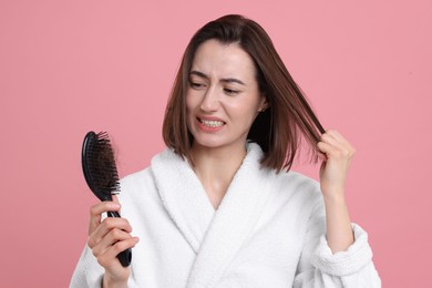 Emotional woman holding brush with lost hair on pink background. Alopecia problem