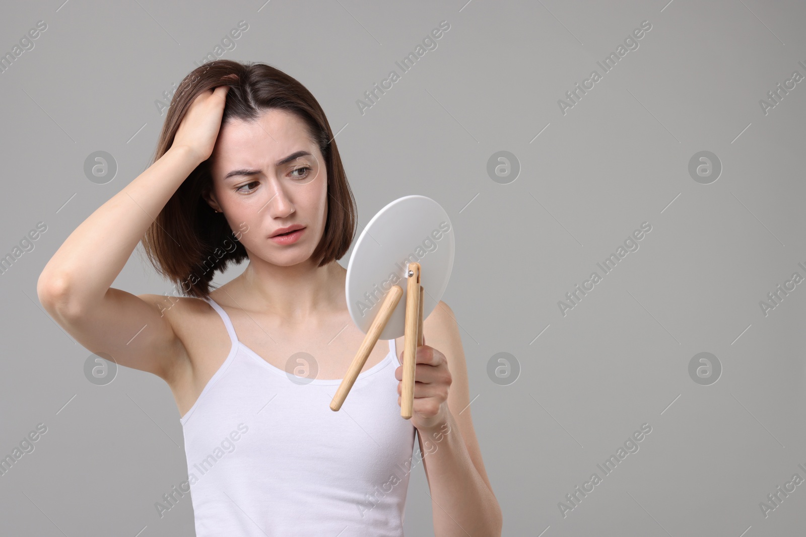 Photo of Sad woman with hair loss problem looking at mirror on grey background. Space for text
