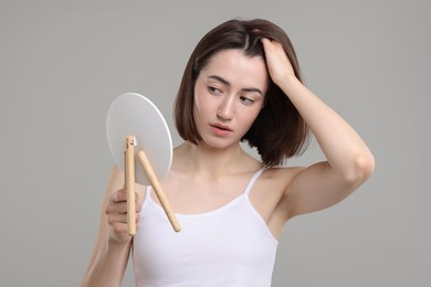 Photo of Sad woman with hair loss problem looking at mirror on grey background