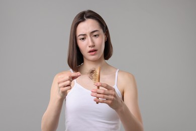 Photo of Stressed woman taking her lost hair from brush on grey background. Alopecia problem