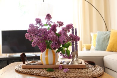 Photo of Beautiful lilac flowers in vase and candles on table at home