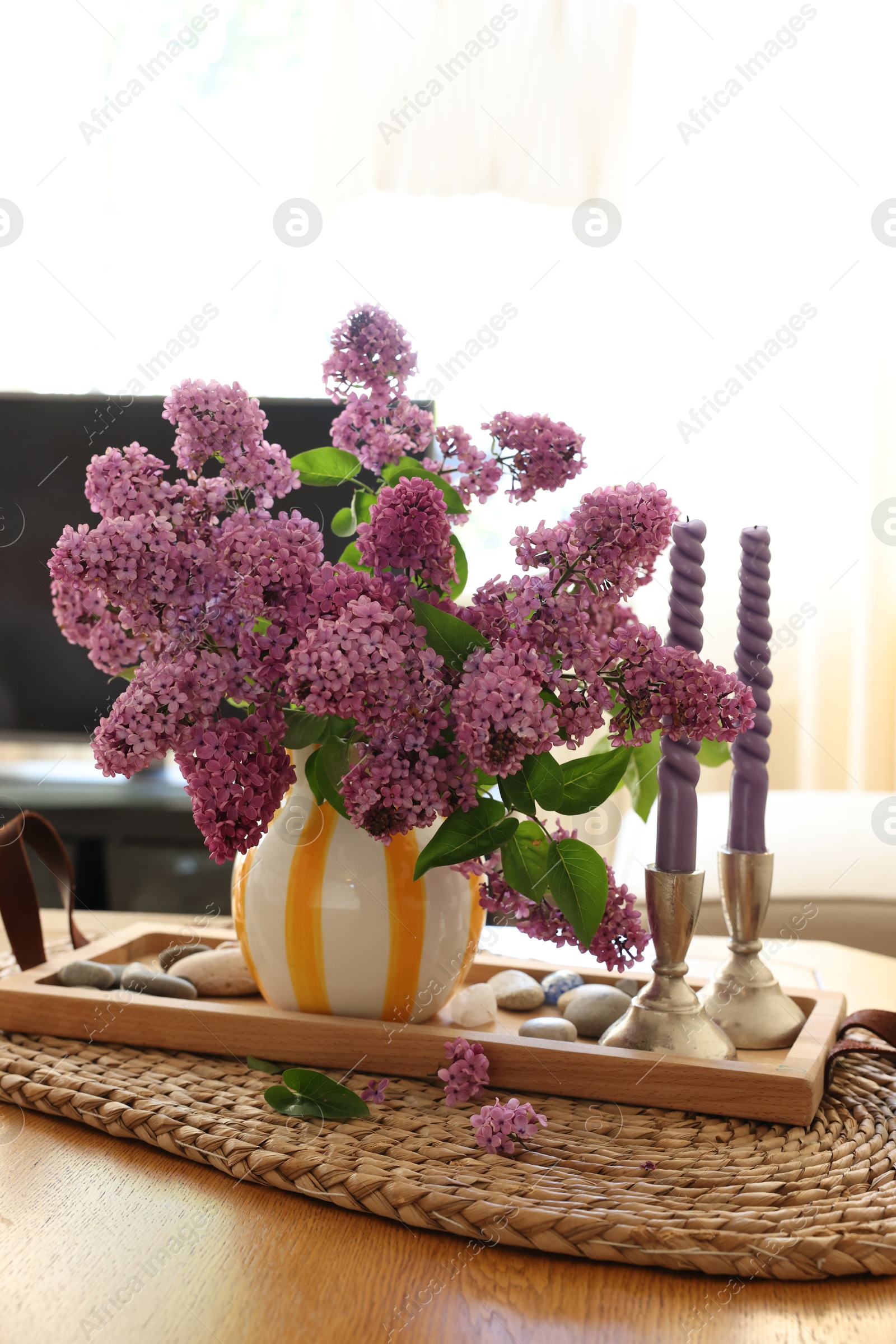 Photo of Beautiful lilac flowers in vase and candles on table at home