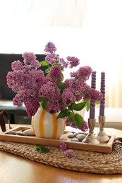 Beautiful lilac flowers in vase and candles on table at home