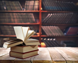 Books on wooden table against shelves in library. Space for text