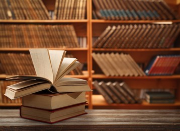 Books on wooden table against shelves in library. Space for text