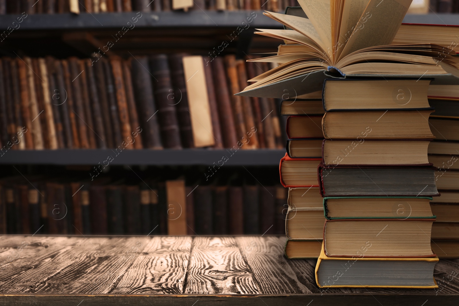 Image of Lots of books on wooden table against shelves in library. Space for text