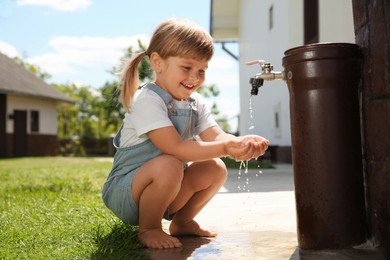 Water scarcity. Cute little girl drawing water with hands from tap outdoors