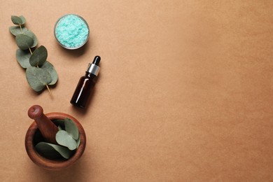 Aromatherapy products. Bottle of essential oil, sea salt, eucalyptus leaves and mortar on brown background, flat lay. Space for text