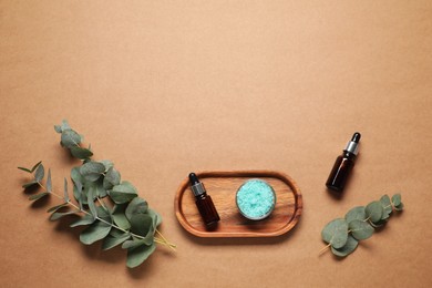 Photo of Aromatherapy products. Bottles of essential oil, sea salt and eucalyptus branches on brown background, flat lay