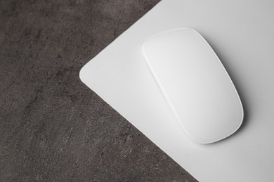 Photo of One wireless mouse with mousepad on black textured table, above view. Space for text