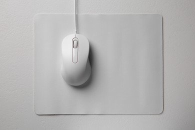 Photo of Wired mouse with mousepad on light textured table, top view