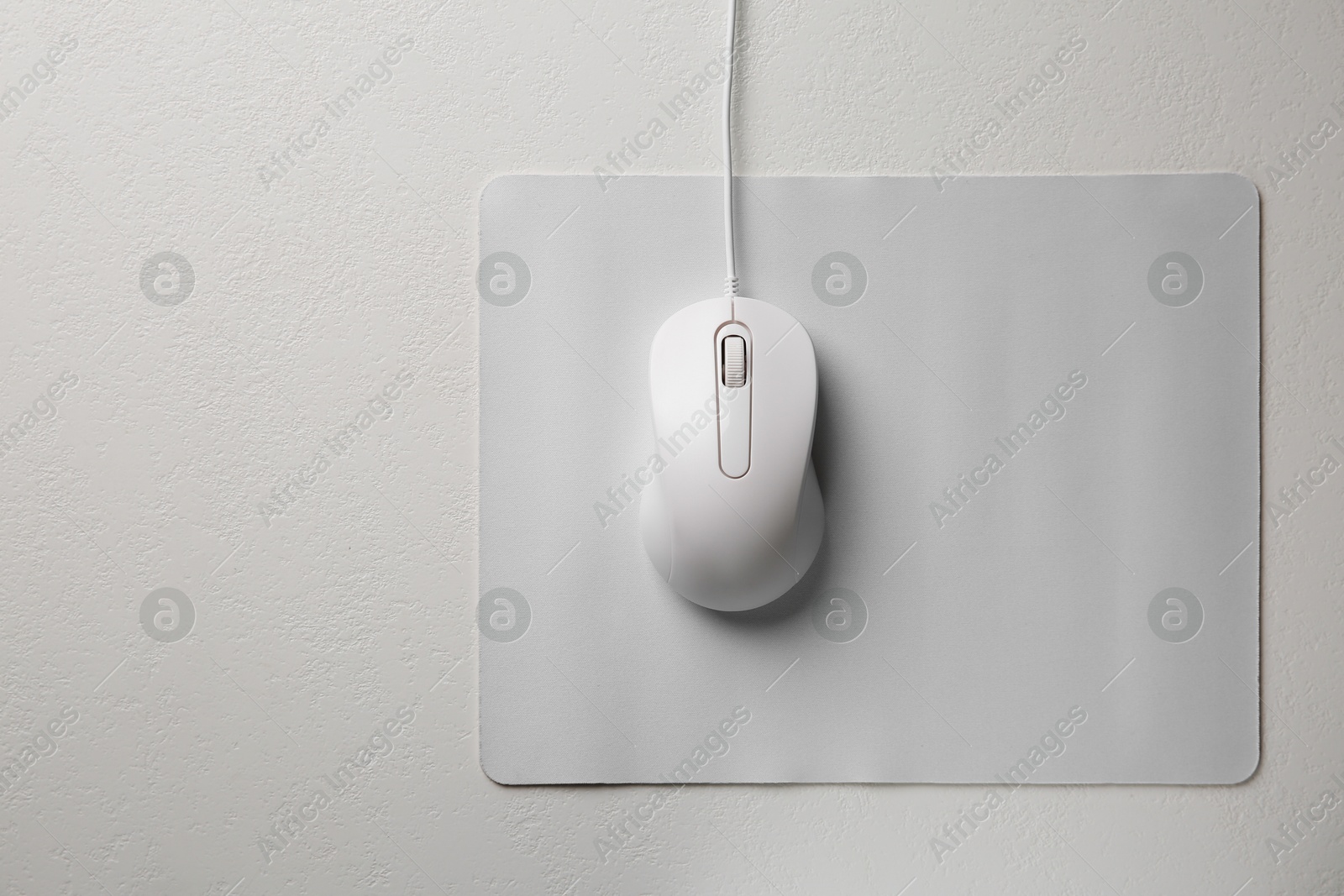 Photo of Wired mouse with mousepad on light textured table, top view. Space for text
