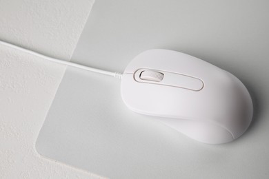 Photo of Wired mouse with mousepad on light textured table, above view