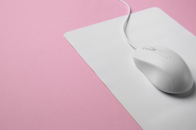 Photo of Wired mouse with mousepad on pink background, closeup. Space for text