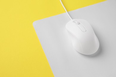 Photo of One wired mouse with mousepad on yellow background, closeup