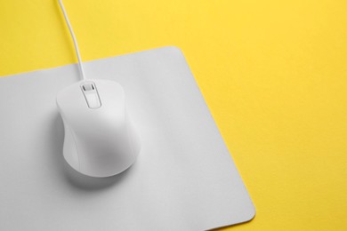 Photo of Wired mouse with mousepad on yellow background, closeup. Space for text