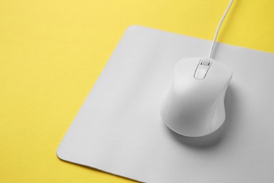 Photo of Wired mouse with mousepad on yellow background, closeup. Space for text