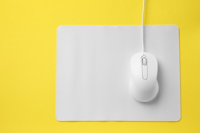 Wired mouse with mousepad on yellow background, top view. Space for text