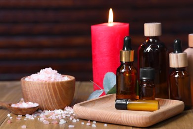 Different aromatherapy products and burning candles on wooden table