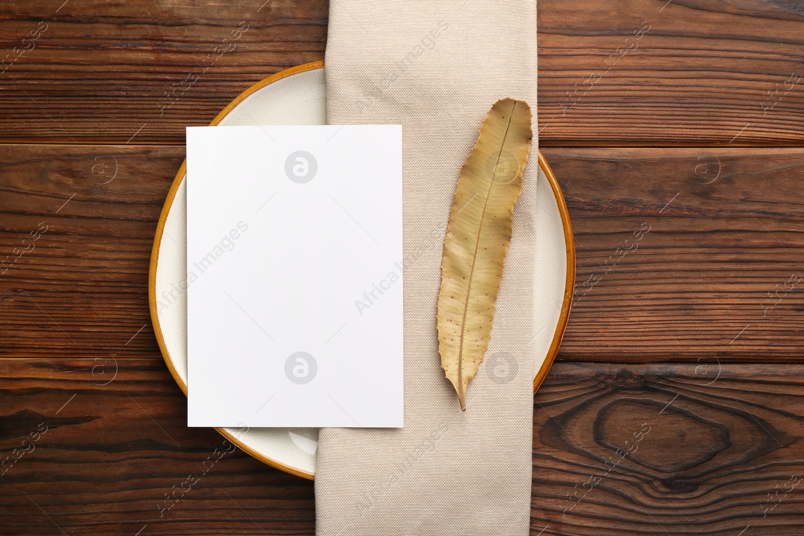 Photo of Empty menu, plate, napkin and dry leaf on wooden table, top view. Mockup for design