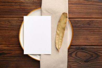 Photo of Empty menu, plate, napkin and dry leaf on wooden table, top view. Mockup for design