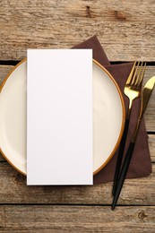 Empty menu, cutlery, plate and napkin on wooden table, top view. Mockup for design