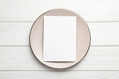 Empty menu and plate on white wooden table, top view. Mockup for design