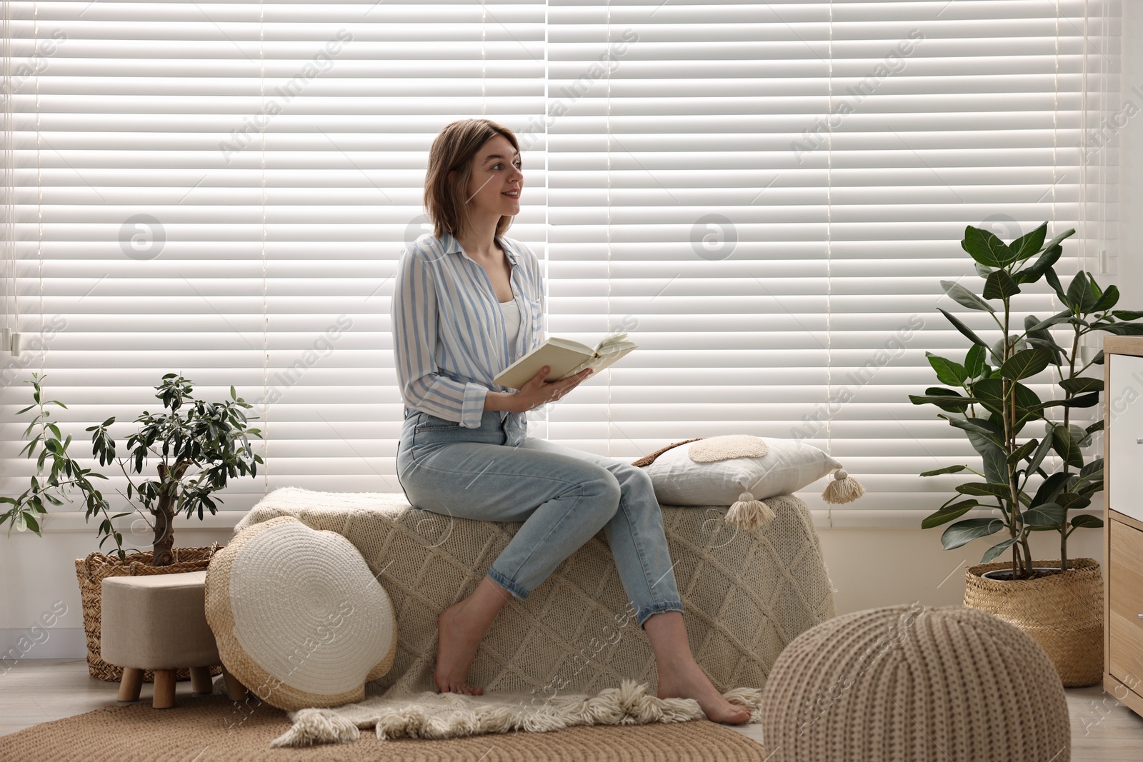 Photo of Woman reading book near window blinds at home