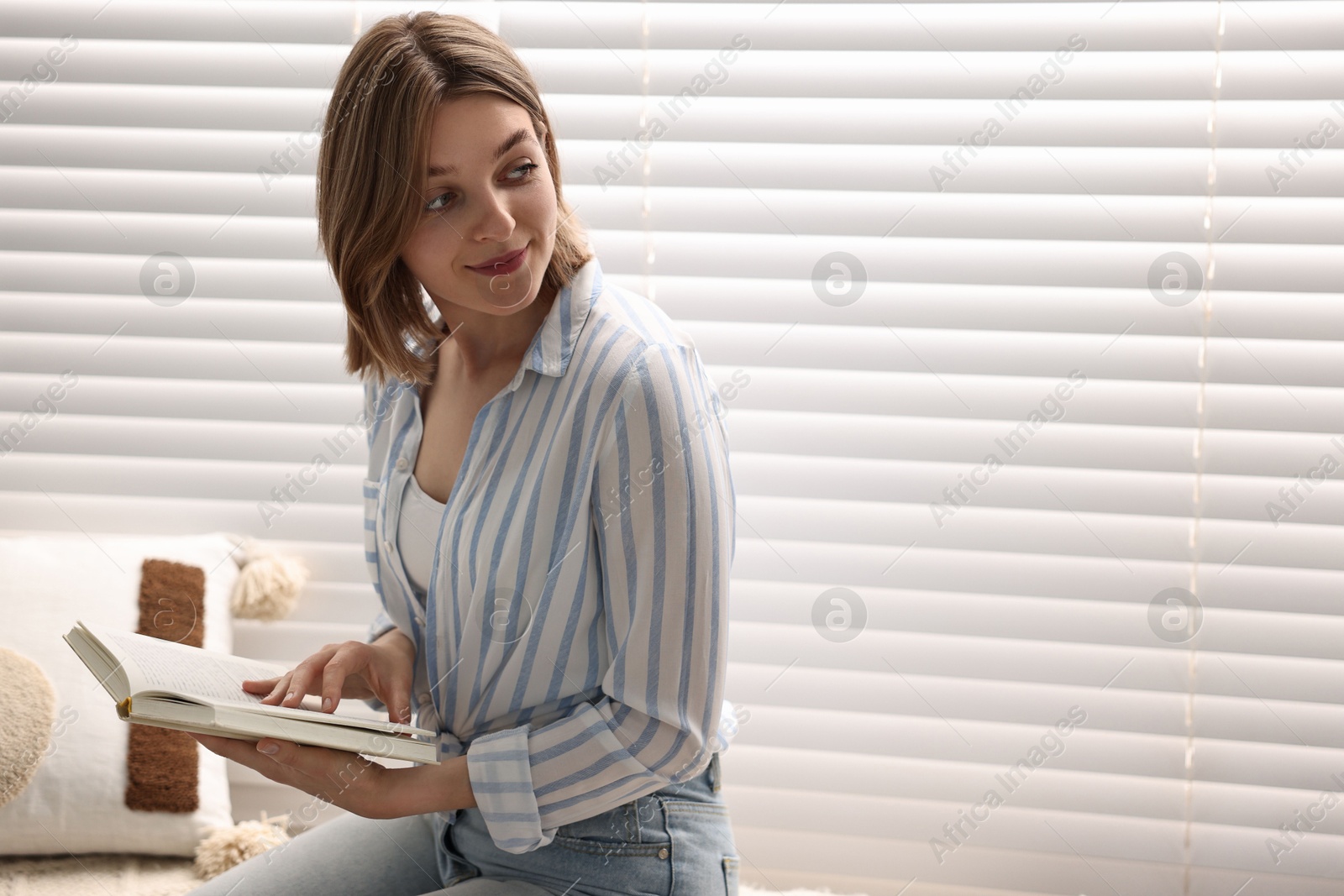 Photo of Woman reading book near window blinds at home, space for text