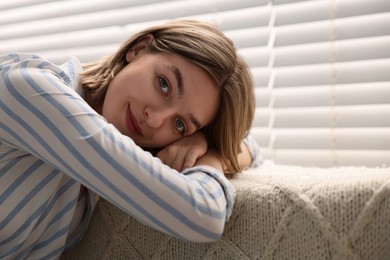 Photo of Young woman relaxing on sofa near window blinds at home