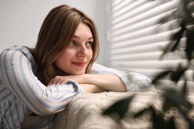 Photo of Young woman relaxing on sofa near window blinds at home