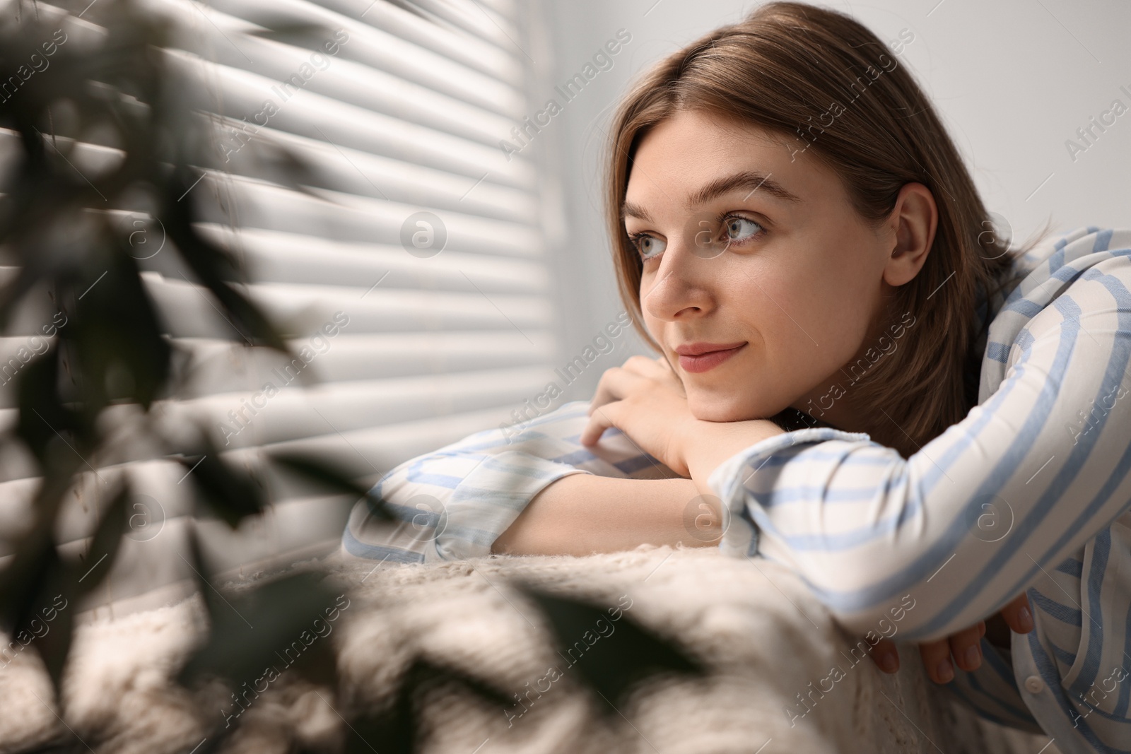 Photo of Young woman relaxing on sofa near window blinds at home