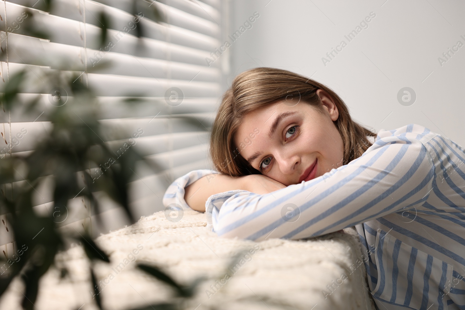 Photo of Young woman relaxing on sofa near window blinds at home