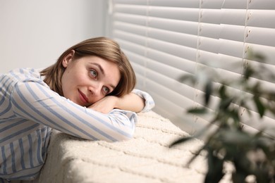 Young woman relaxing on sofa near window blinds at home