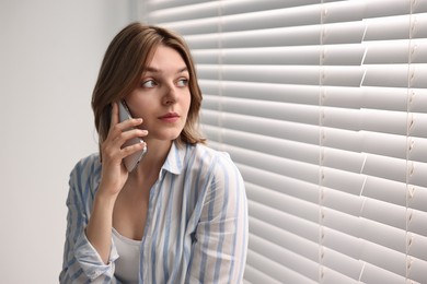 Woman talking on phone near window blinds at home, space for text