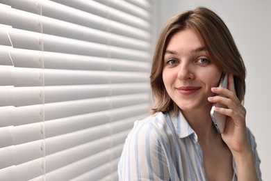 Woman talking on phone near window blinds at home, space for text
