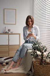 Photo of Woman using phone near window blinds at home
