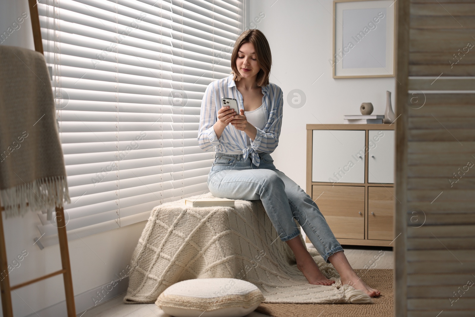 Photo of Woman using phone near window blinds at home