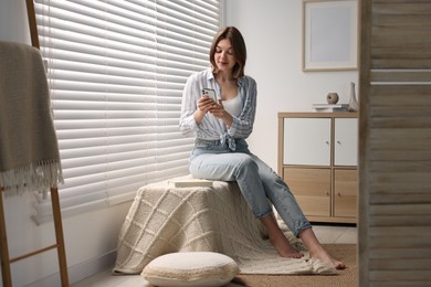 Woman using phone near window blinds at home