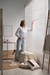 Young woman near window blinds at home