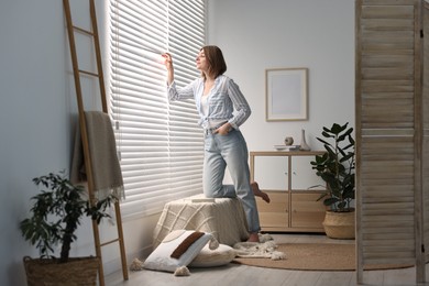 Young woman near window blinds at home