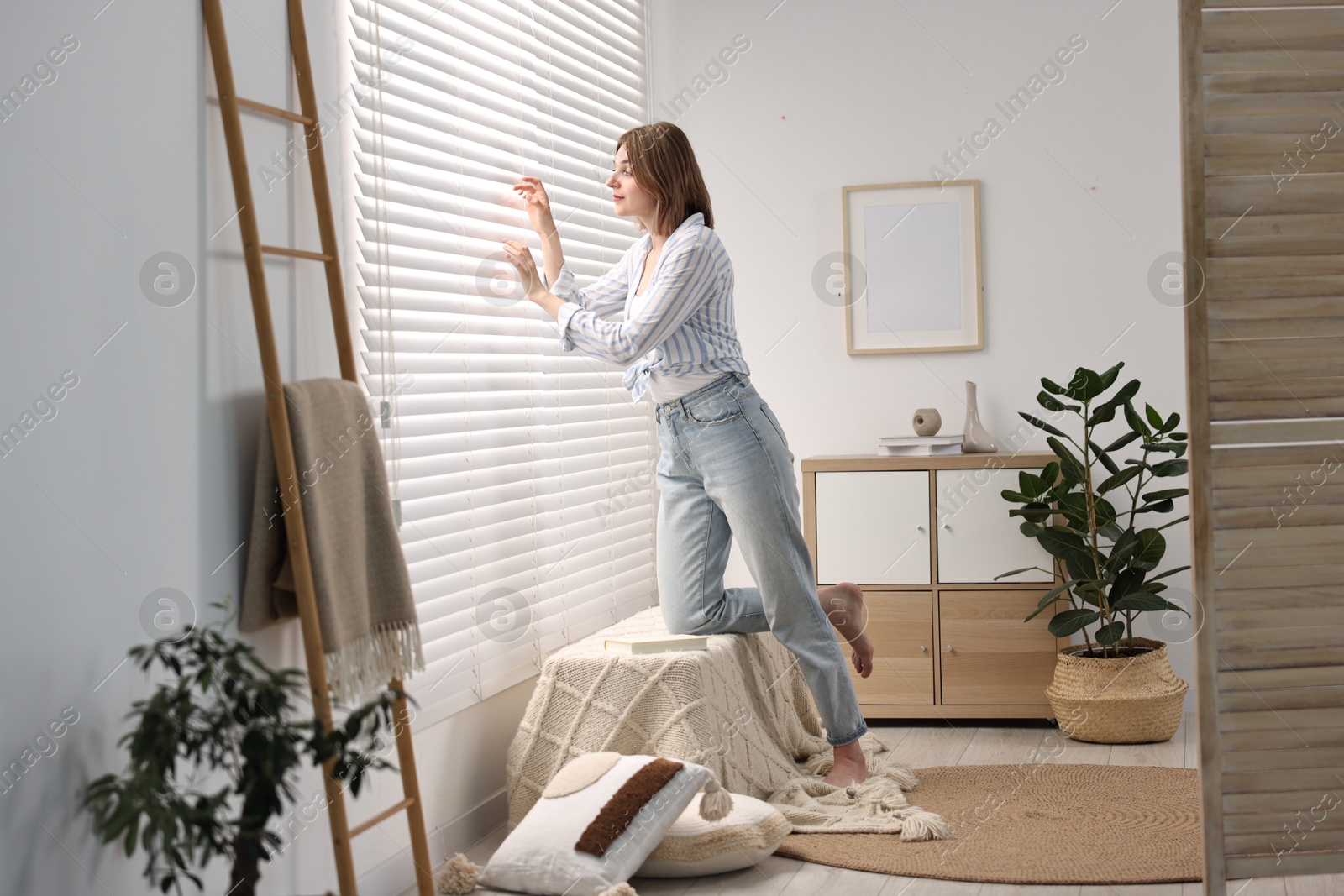 Photo of Young woman near window blinds at home