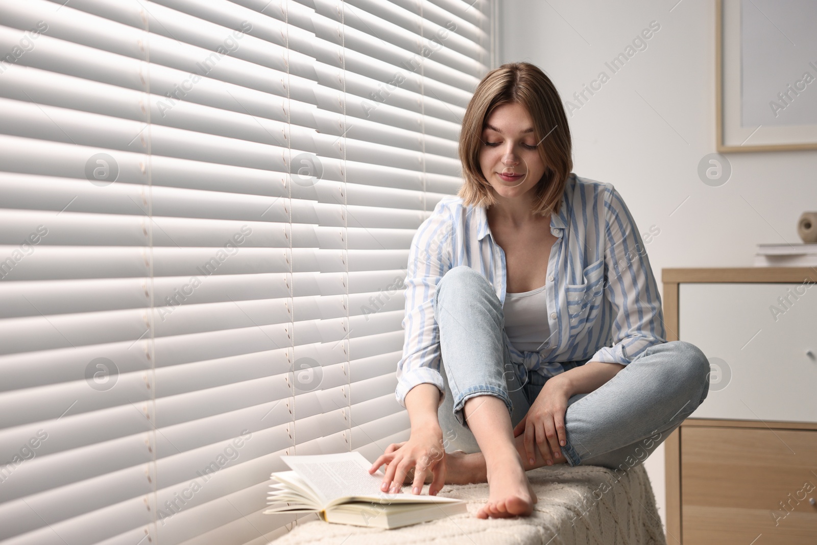 Photo of Young woman near window blinds at home