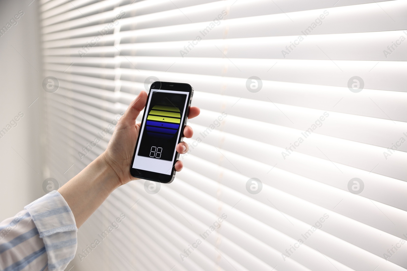 Photo of Woman using smartphone to adjust window blinds indoors, closeup. Space for text