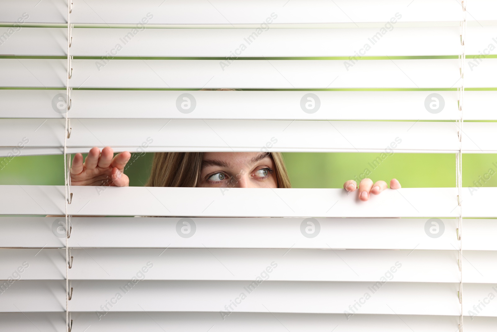 Photo of Young woman looking through window blinds on blurred background