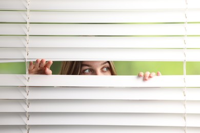 Photo of Young woman looking through window blinds on blurred background