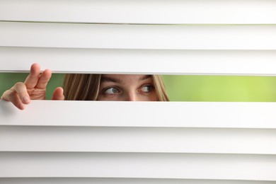 Photo of Young woman looking through window blinds on blurred background, space for text
