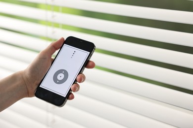 Woman using smartphone to adjust window blinds indoors, closeup. Space for text